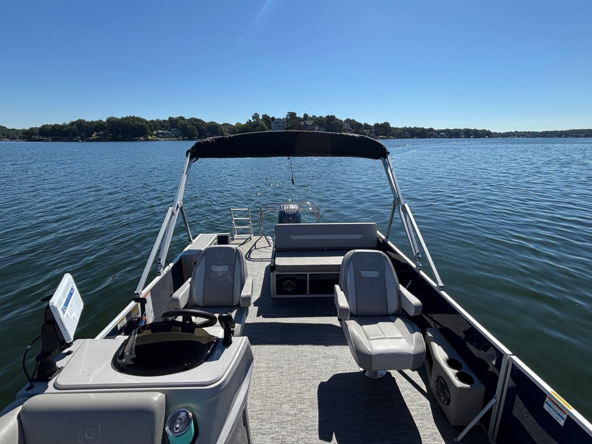 A pontoon boat interior with seats on a lake under a clear blue sky.