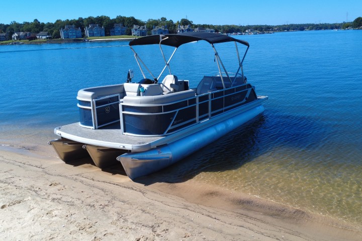 Pontoon boat on sandy shore with calm blue water and houses in the background.