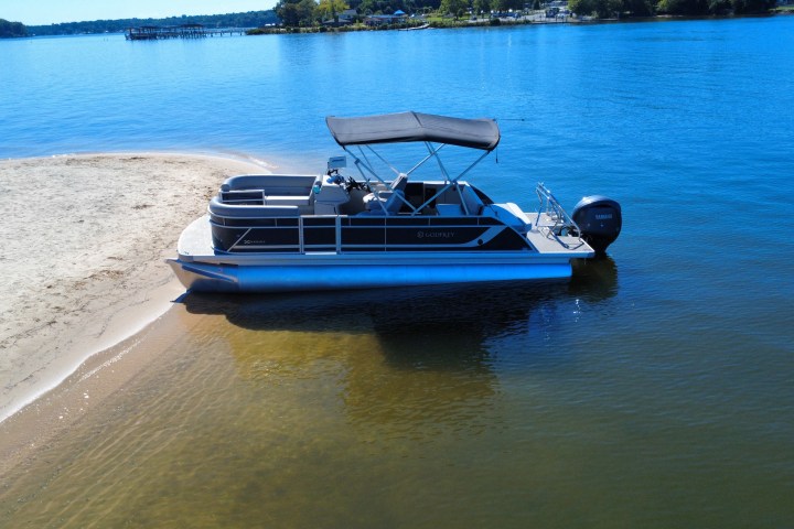 Pontoon boat anchored on sandy beach, under clear blue sky on a sunny day.